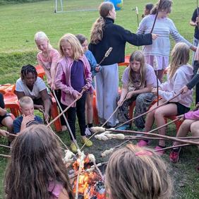 Kinder sitzen am Lagerfeuer und machen Stockbrot