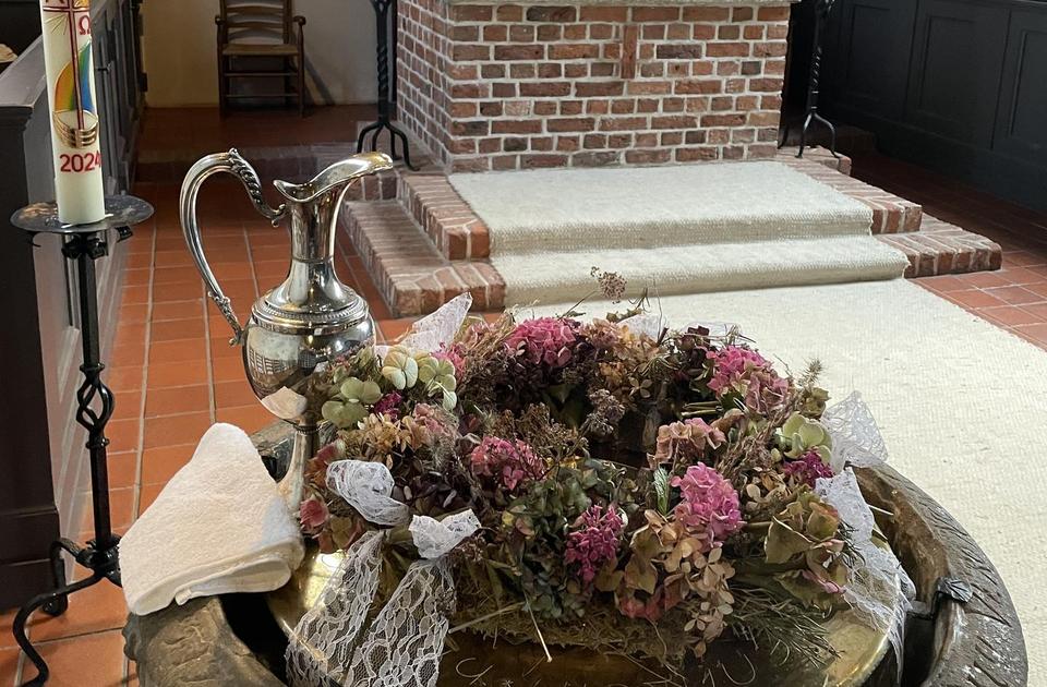 Im Vordergrund ist das Taufbecken der Kirche zu sehen, hinten der Altar.